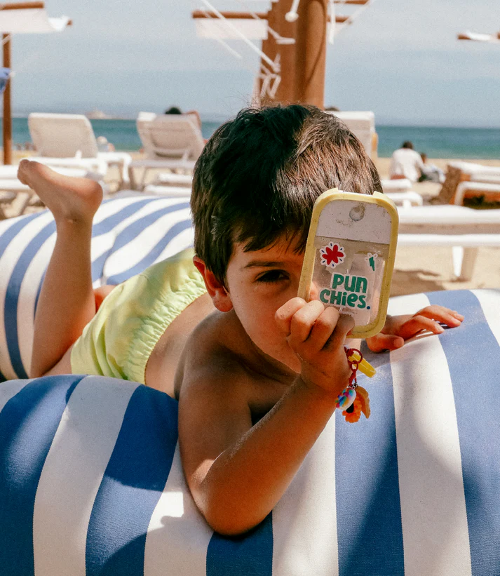 Criança deitada na praia num colchão azul e branco riscado