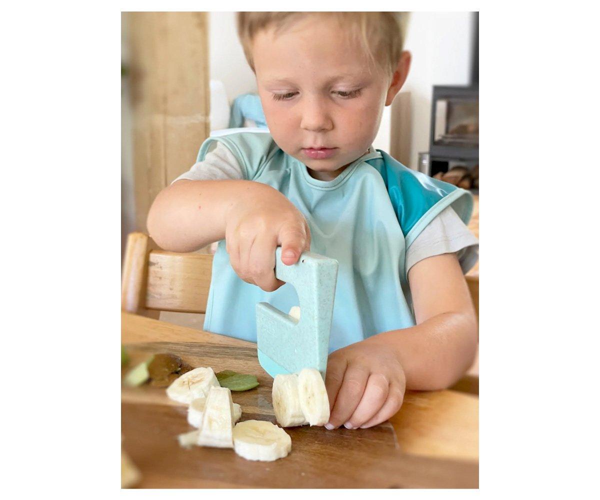Criança a cortar banana com faca de plástico azul no interior