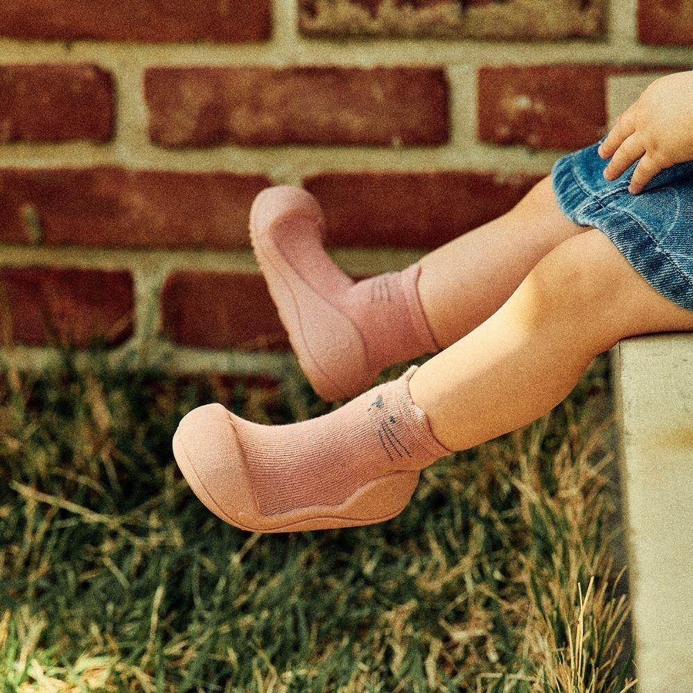 Meias cor-de-rosa com sola em criança junto a muro de tijolos e relva