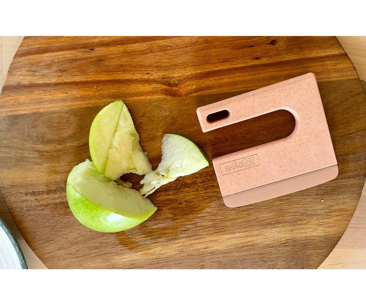 Peça rosa com a marca MAACOM e maçã verde partida sobre tábua de madeira.