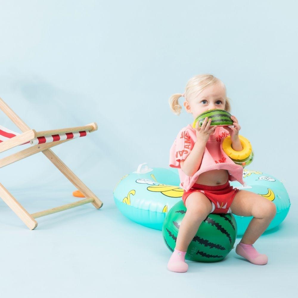 Criança com brinquedos de fruta sentada em balão insuflável verde com padrão de melância
