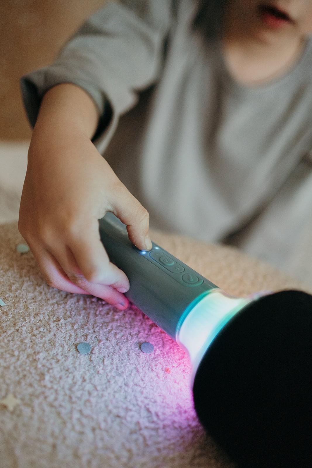 Microfone de brinquedo cinza com luzes coloridas na mão de criança sobre superfície felpuda.