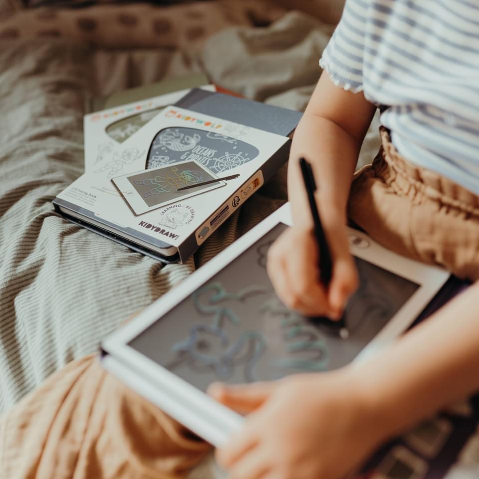 Tablet de desenho digital branco com caneta preta e duas embalagens brancas ao lado