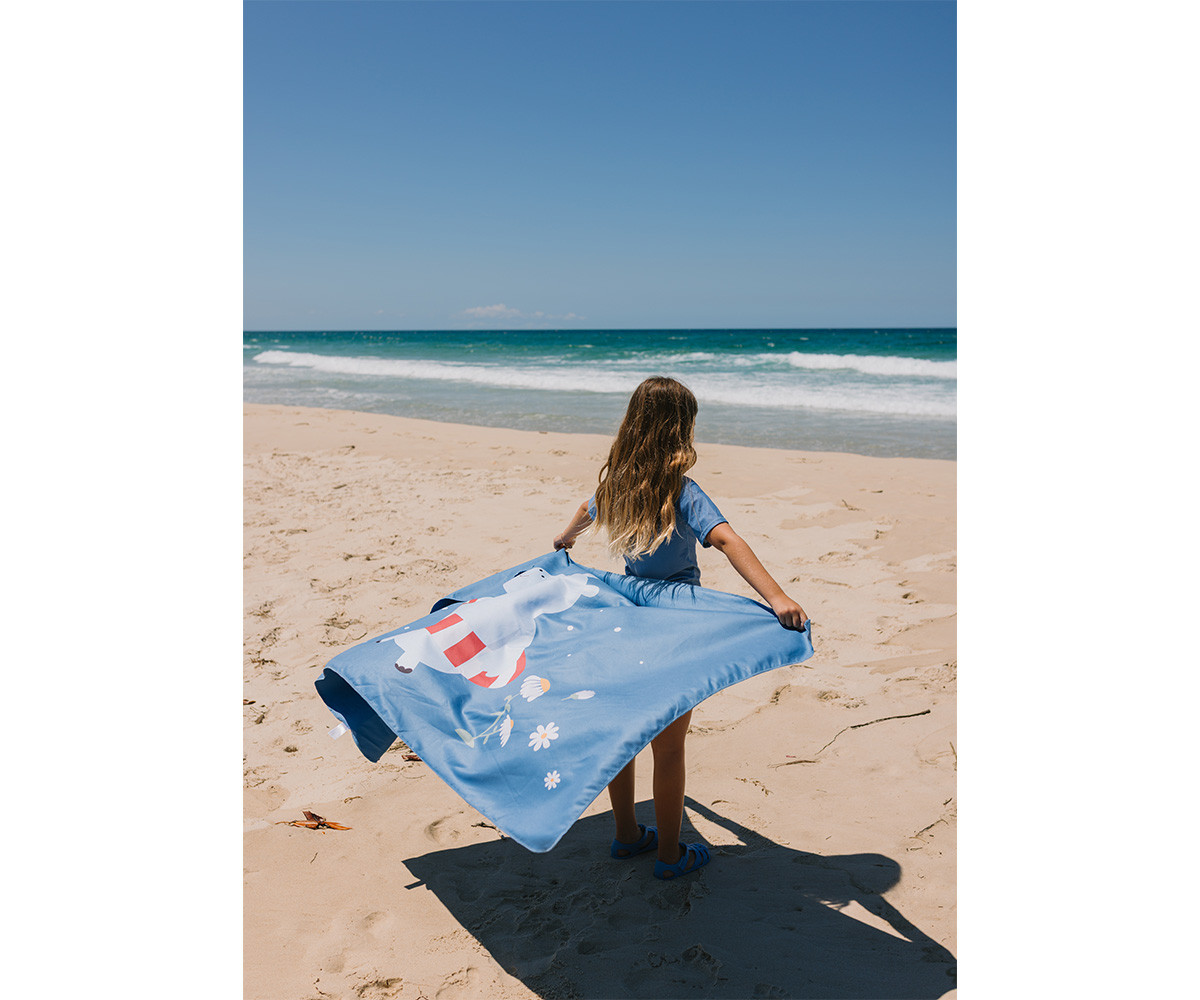 Criança na praia com toalha azul com desenho de urso branco e flores