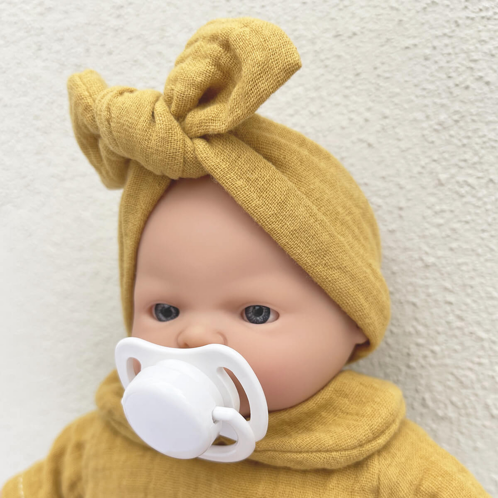 Boneca com chupeta branca e roupa amarela mostarda com faixa na cabeça