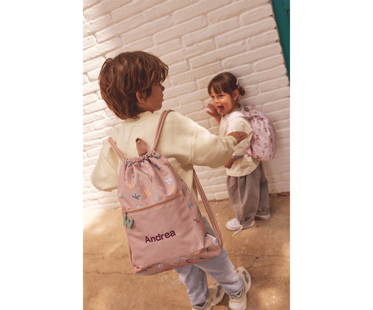 Duas crianças com sacos de cordão cor-de-rosa personalizados contra parede branca