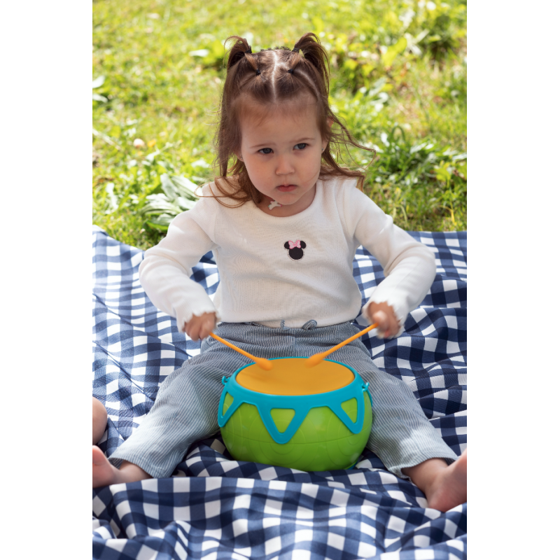 Criança a tocar tambor verde com pele laranja num cobertor azul e branco