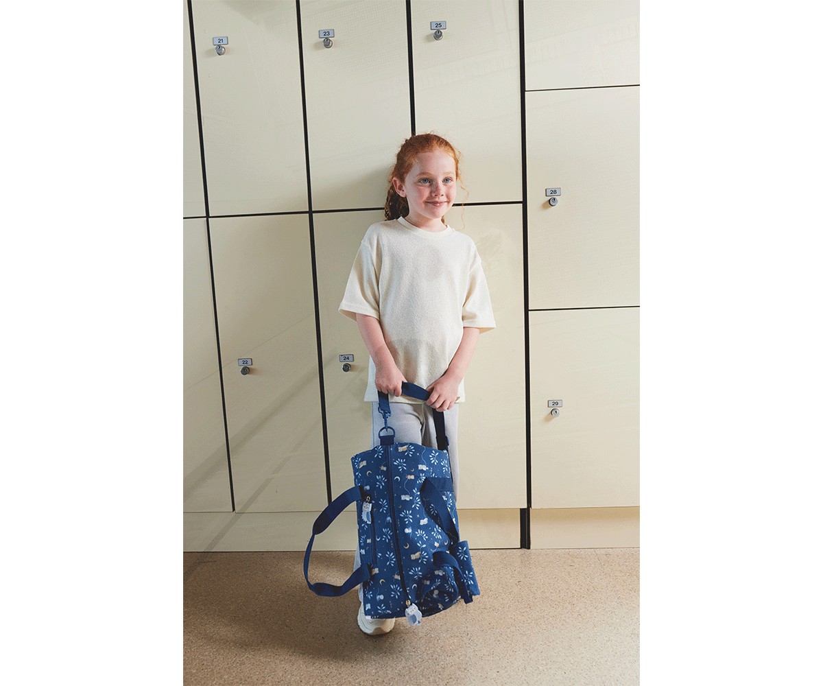 Criança com mochila azul floral em frente a armários escolares creme