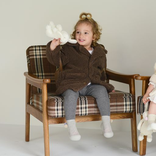Criança com casaco felpudo castanho sentada em cadeira de madeira com almofadas xadrez