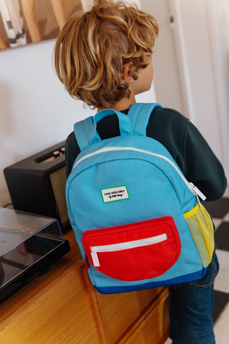 Mochila infantil azul, vermelho e amarelo com etiqueta, vista de costas num menino