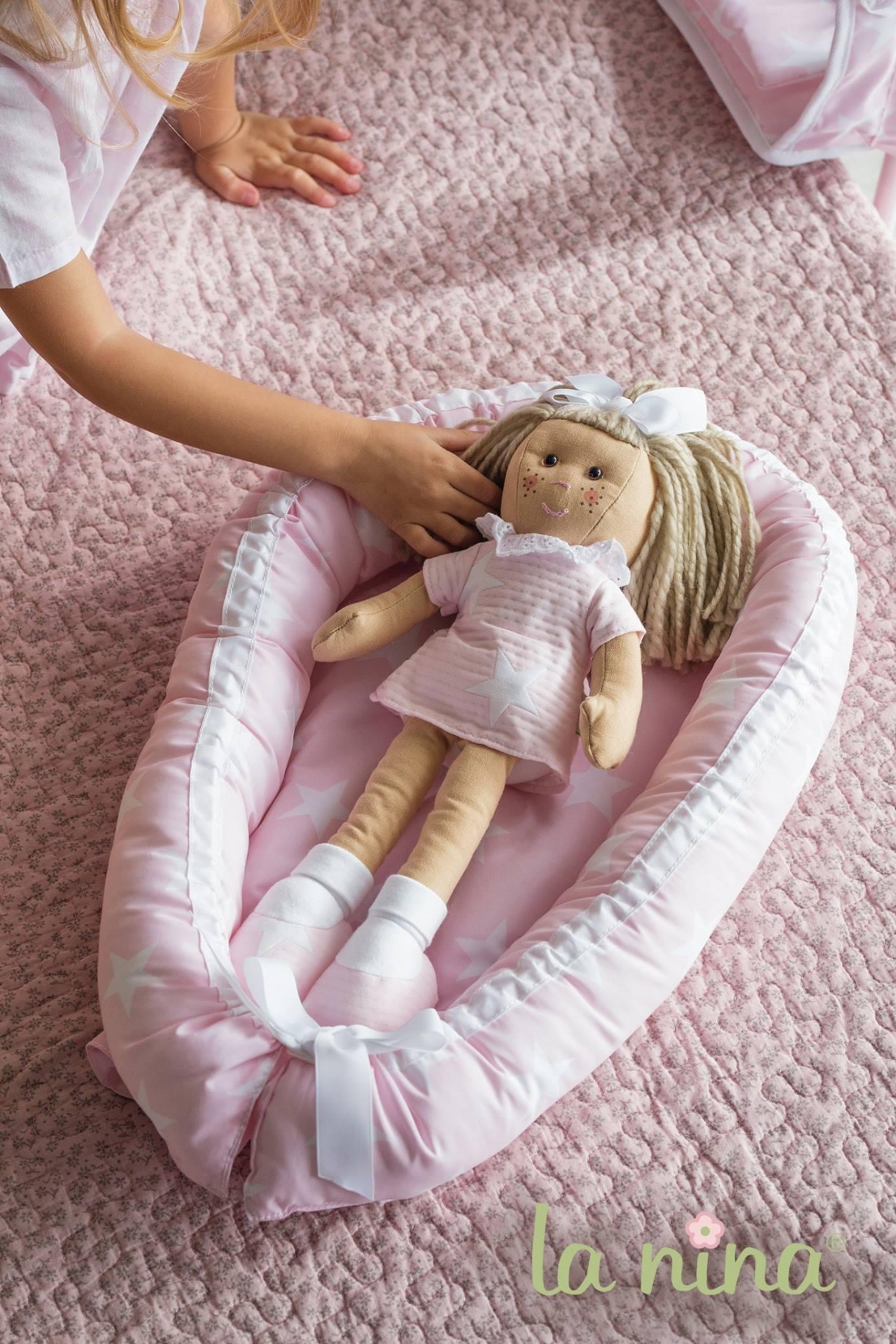 Boneca de tecido rosa num suporte acolchoado cor-de-rosa sobre manta rosa acolchoada