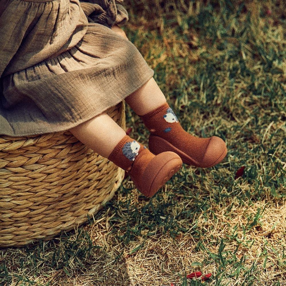 Botas castanhas para bebé com meias decoradas com raposas sentada numa cesta de palha