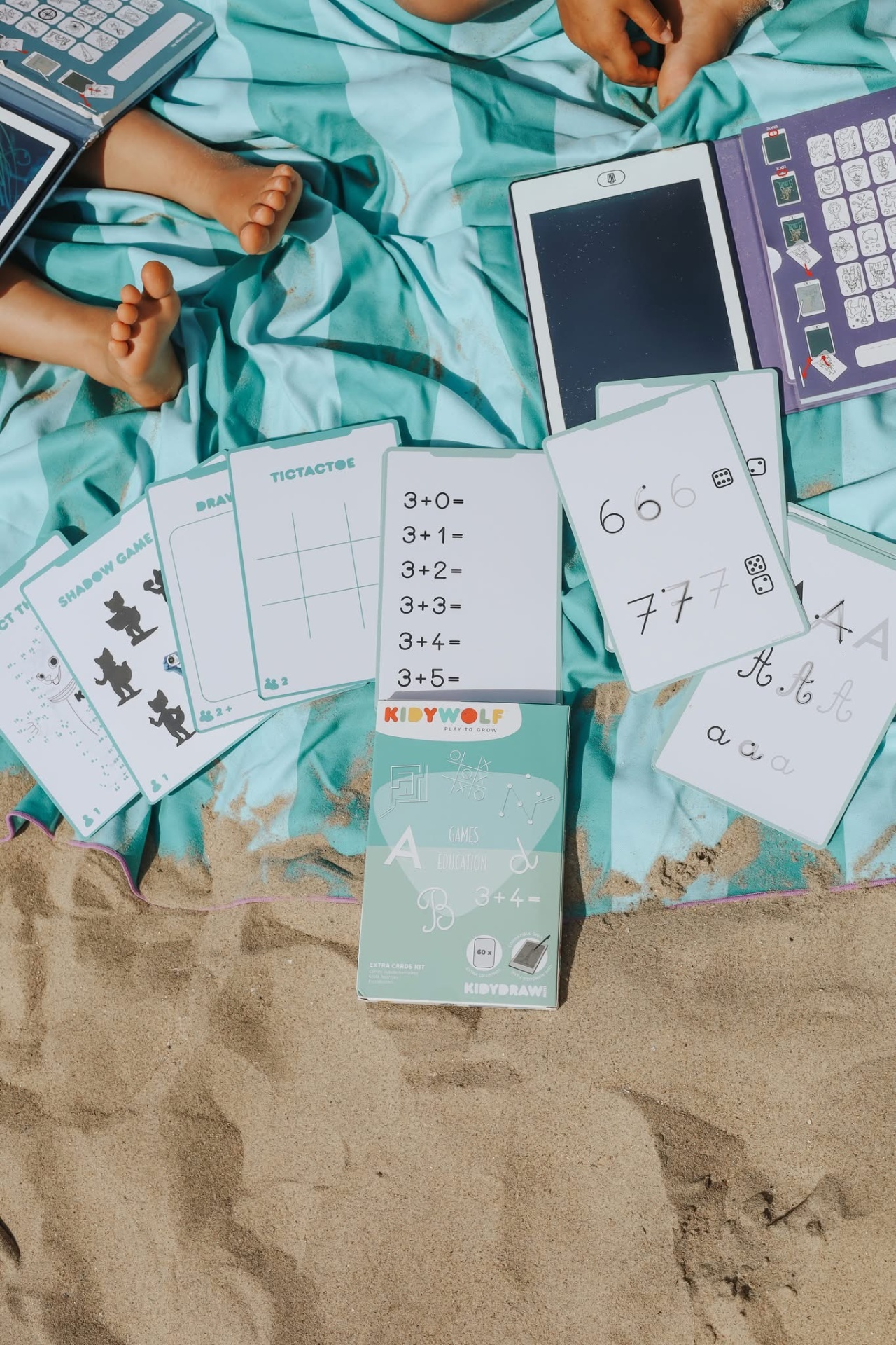 Cartas educativas KIDYWOLF com temas de matemática e escrita numa toalha azul clara na areia