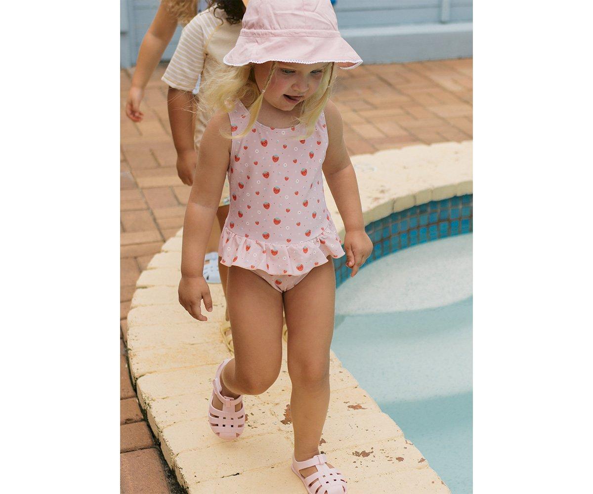 Criança com fato de banho rosa e chapéu junto a piscina