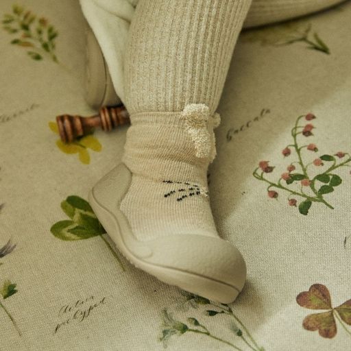 Sapato infantil cinza com meia creme de padrão animal sobre tecido com padrão floral