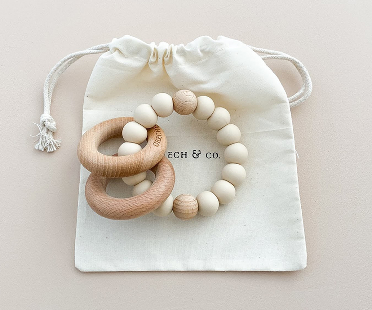 Brinquedo para bebés com anéis de madeira e contas de silicone em saco branco.