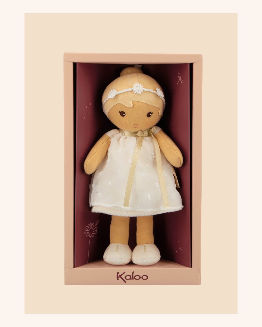 Boneca de pano Kaloo vestida com vestido branco em caixa rosa.