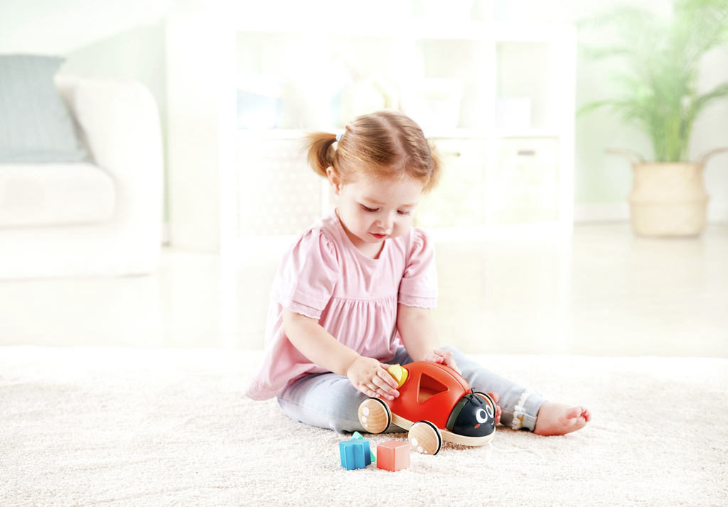 Menina pequena a brincar com brinquedo de madeira vermelho em forma de carrinho no tapete