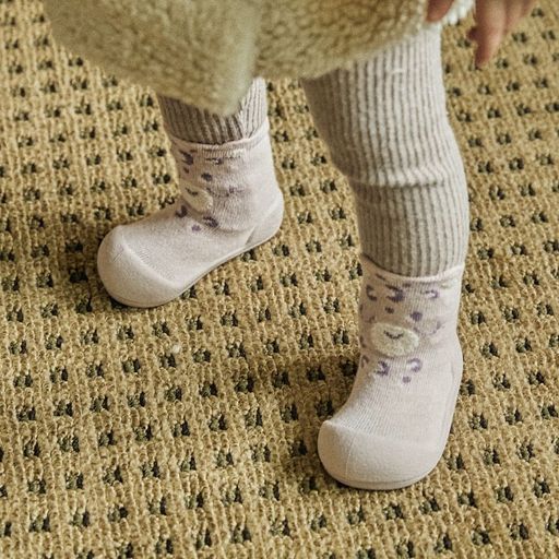 Meias-calçado creme com padrão de onça usadas por bebé sobre tapete bege