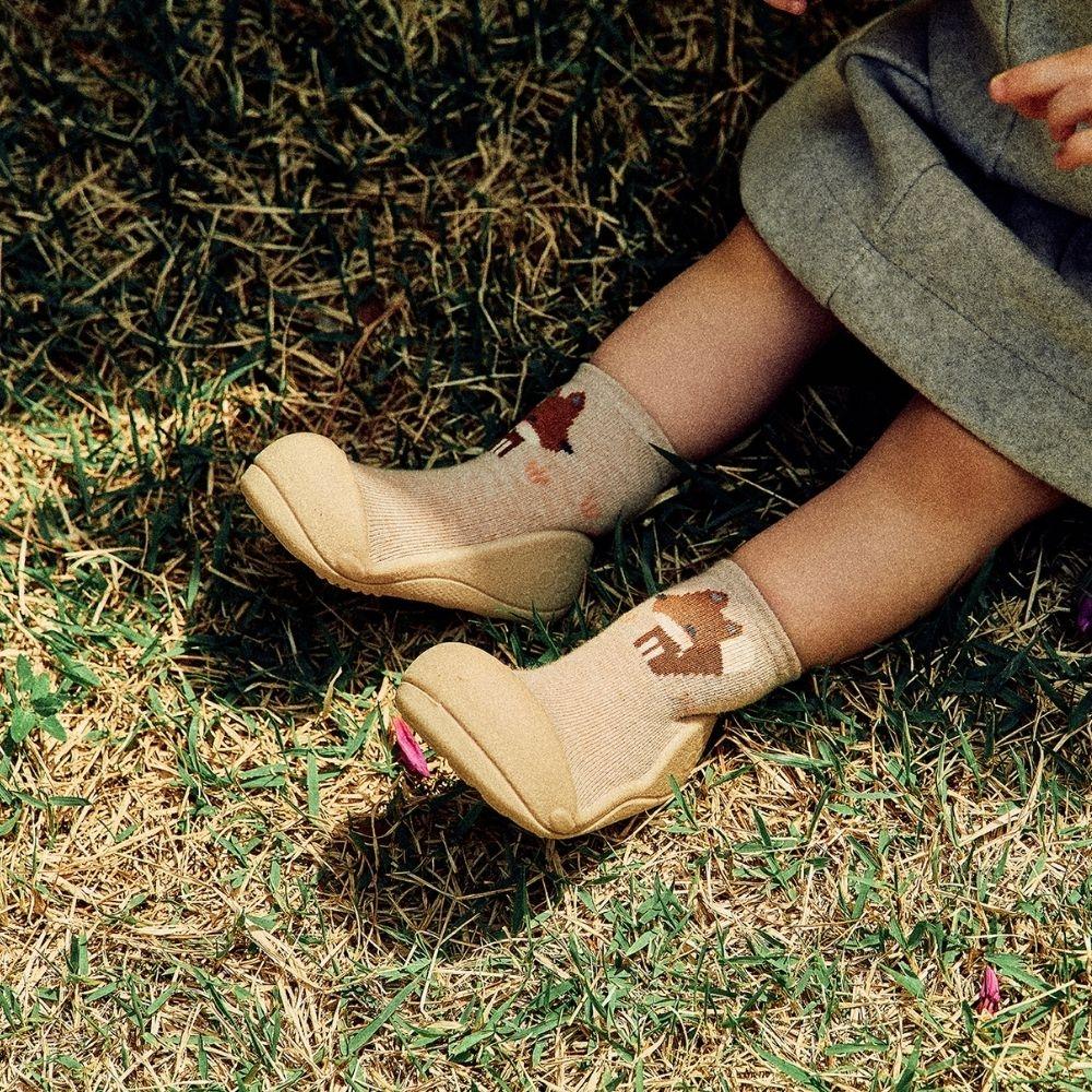 Sapatos infantis bege com meias bege e padrão marrom, criança sentada na relva