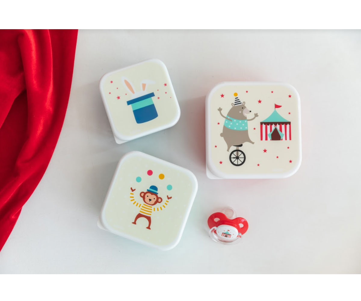 Três caixas brancas com desenhos coloridos de circo e uma chupeta vermelha sobre fundo branco e tecido vermelho