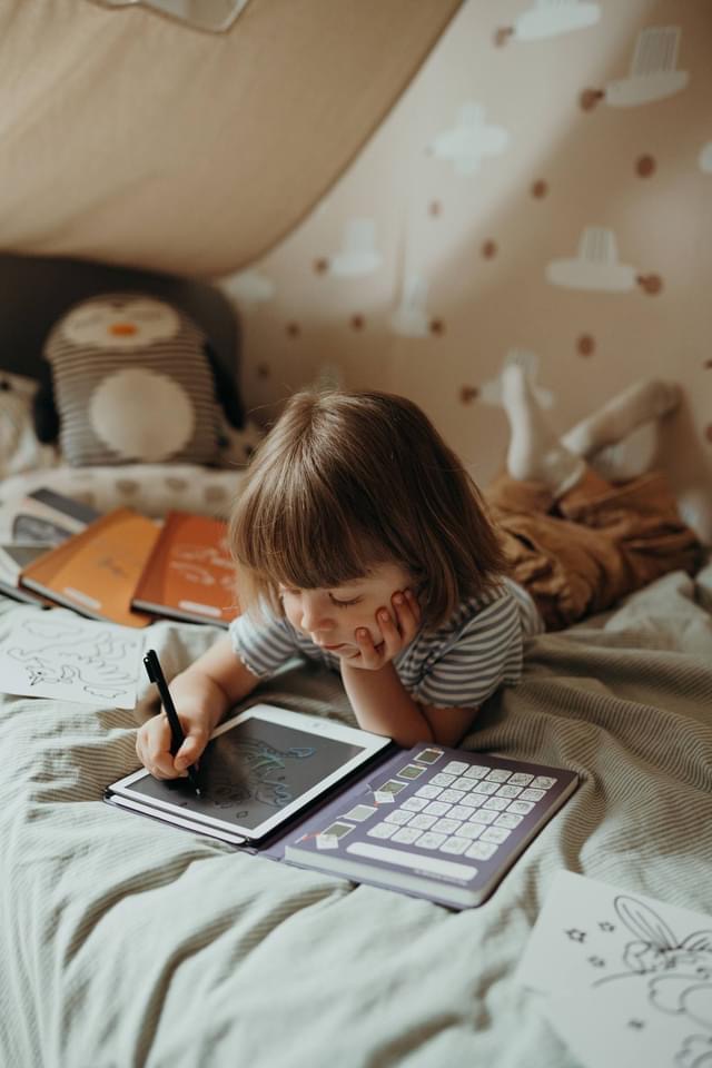Criança a desenhar numa tablet num quarto infantil com almofada de pinguim e parede decorada