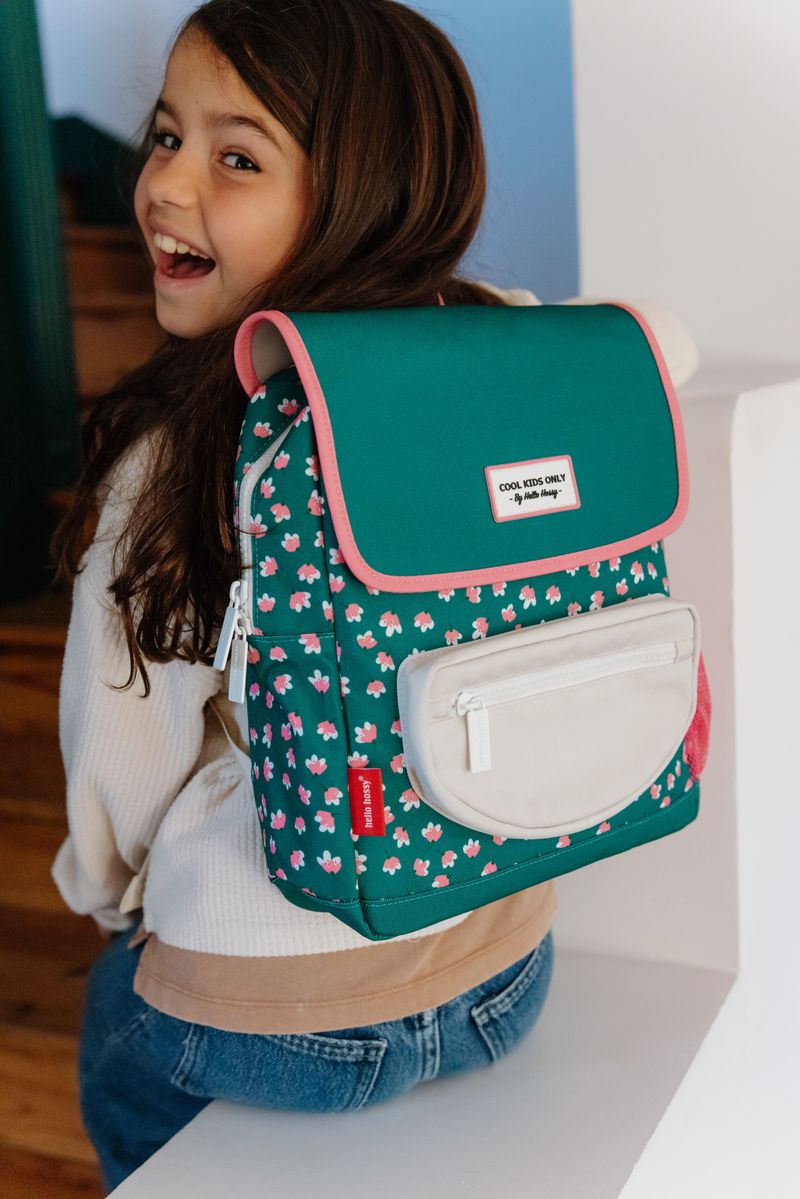 Mochila verde com flores cor-de-rosa e bolso bege, usada por criança sorridente