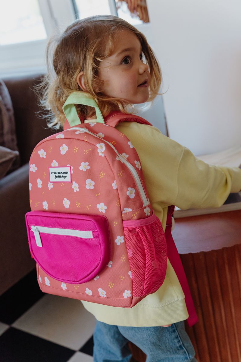 Mochila infantil rosa com flores brancas e bolso rosa forte vista de lado com criança a usá-la.
