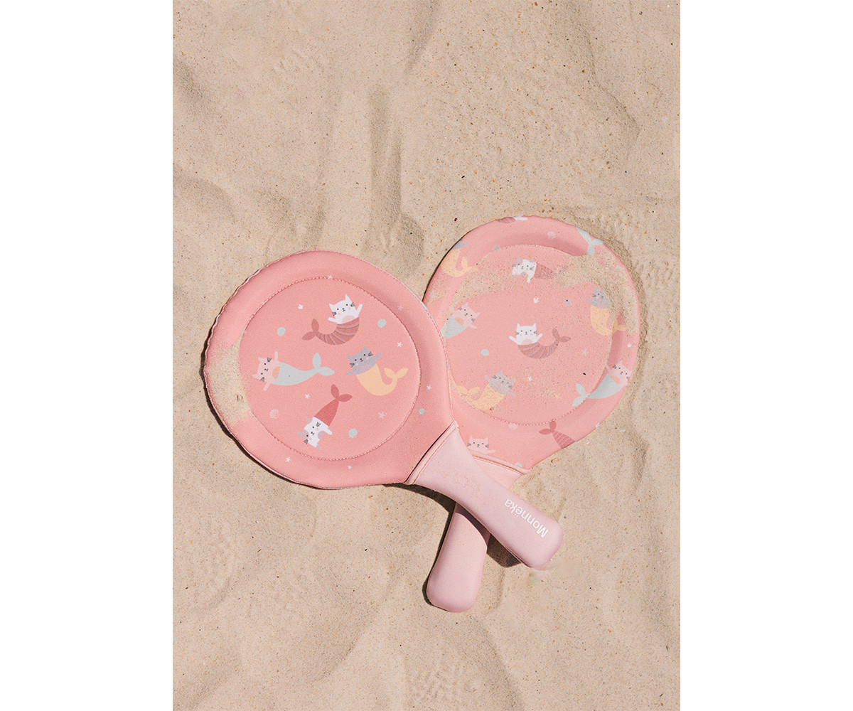 Duas raquetes de praia cor-de-rosa com padrão de gatos sereia sobre areia.