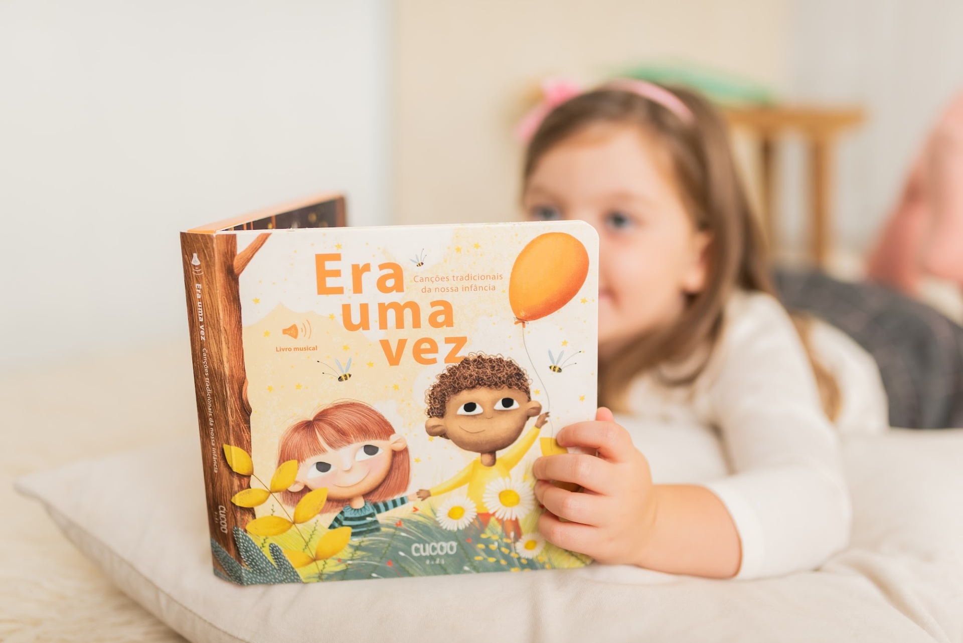 Criança deitada segurando um livro infantil intitulado Era uma vez com ilustrações coloridas