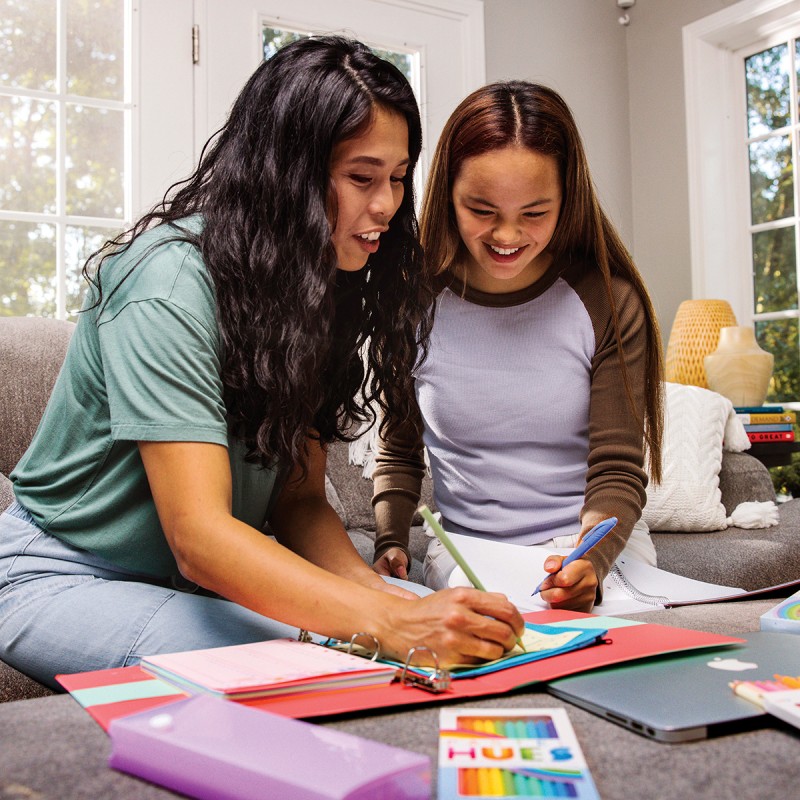 Duas raparigas a estudar numa mesa com cadernos coloridos e lápis de cor
