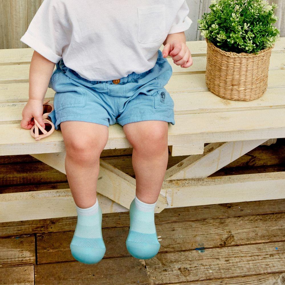 Criança sentada em banco de madeira com roupa azul e branca e planta ao lado