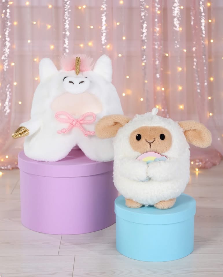 Peluches de unicórnio e ovelha sobre caixas redondas coloridas com fundo iluminado