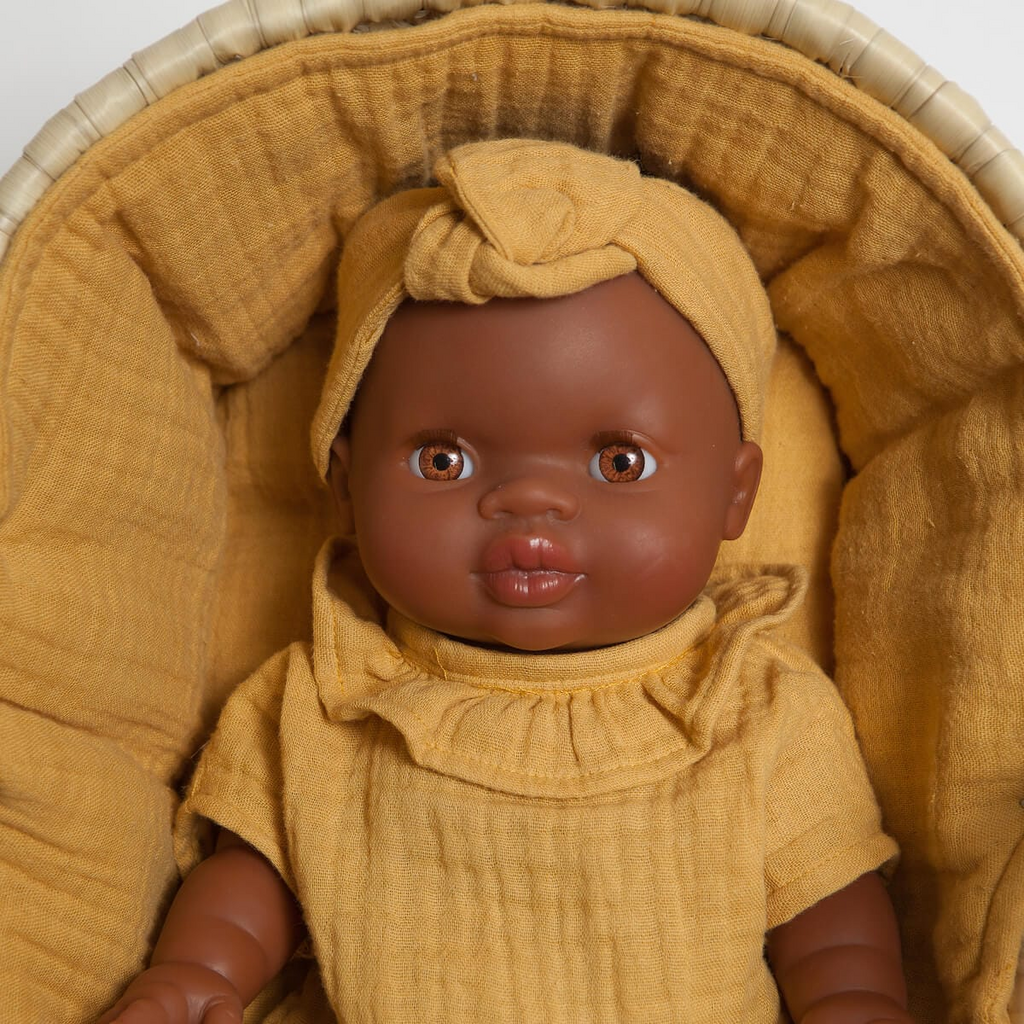 Boneca bebé com roupa e turbante mostarda numa almofada acolchoada da mesma cor