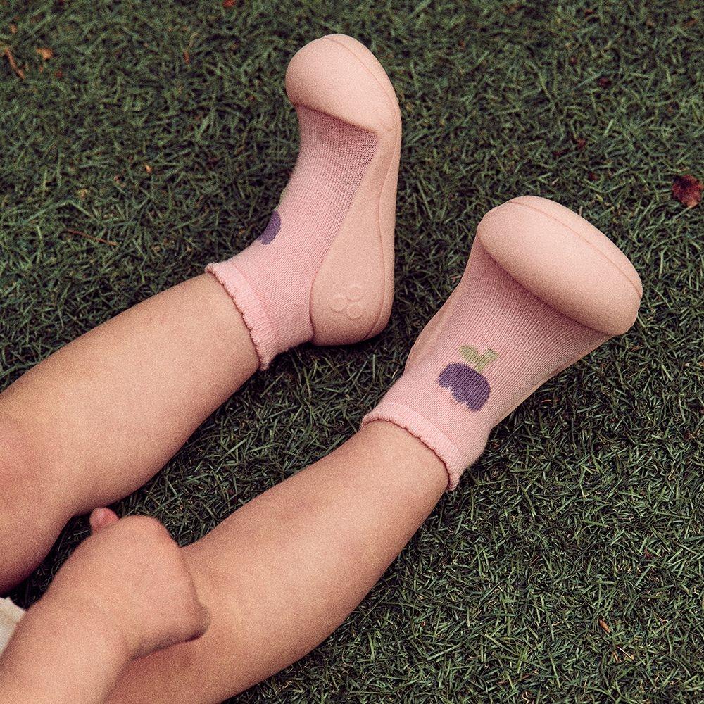 pés de criança com meias cor-de-rosa decoradas com uvas e sapatos de borracha rosa claro na relva