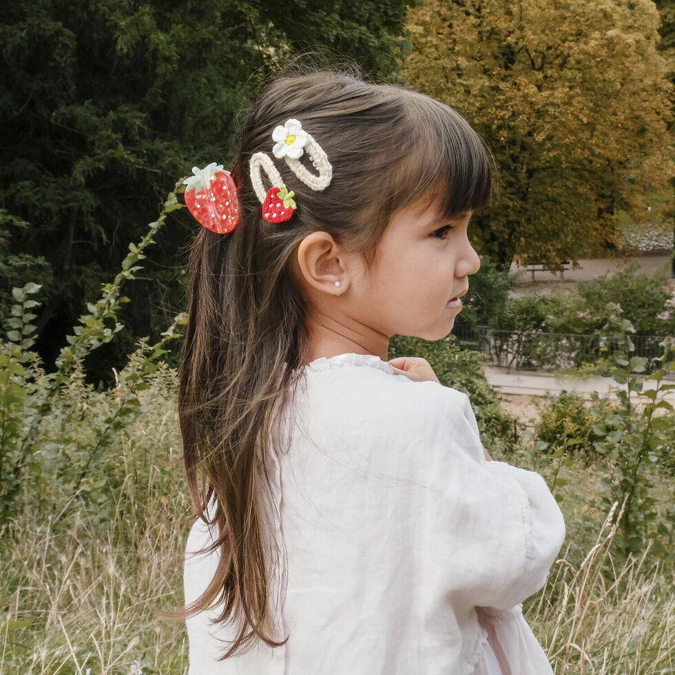 criança com presilhas de cabelo de morango e flor ao ar livre