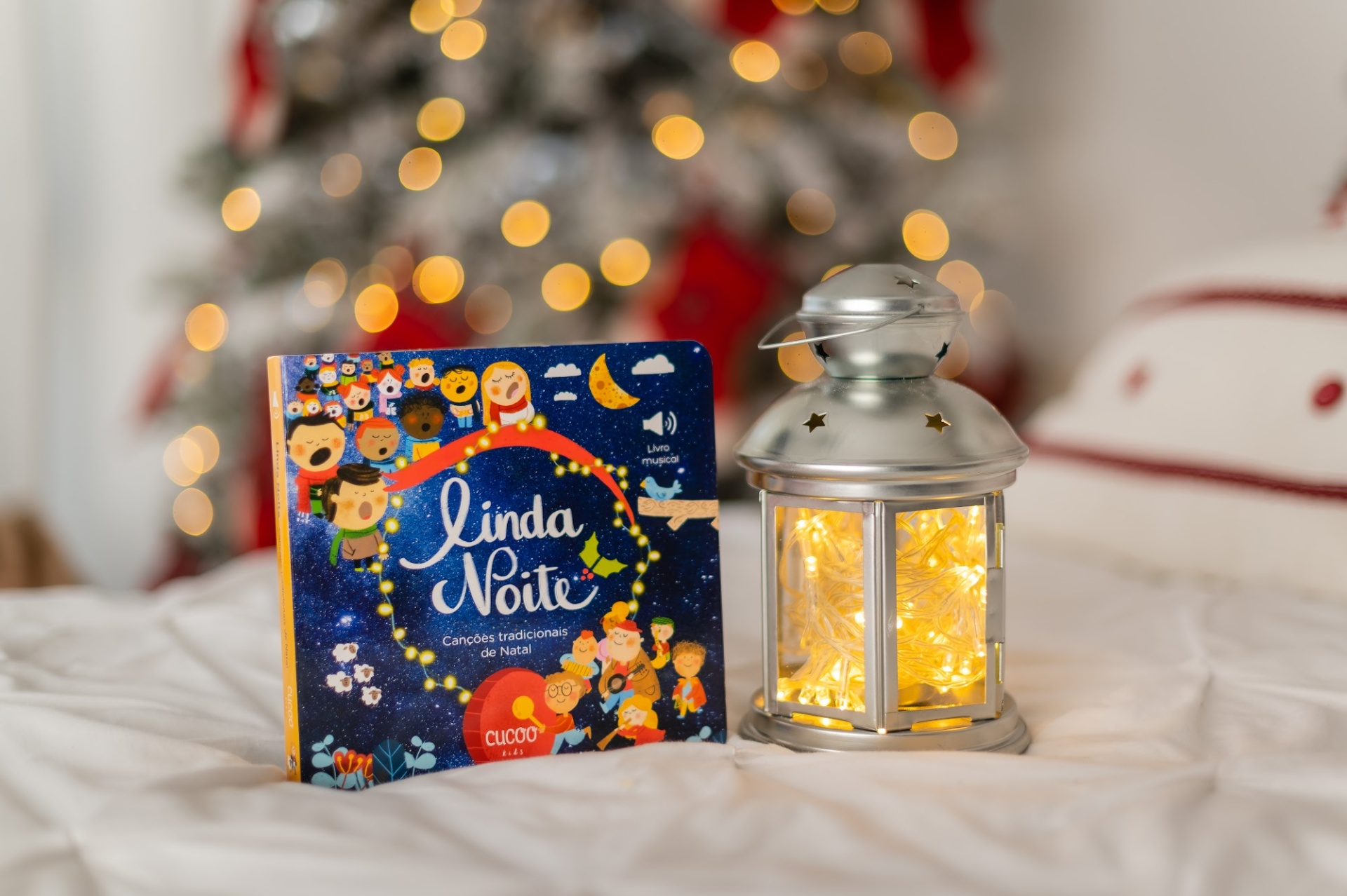 Livro infantil 'Linda Noite' ao lado de lanterna iluminada num cenário de Natal