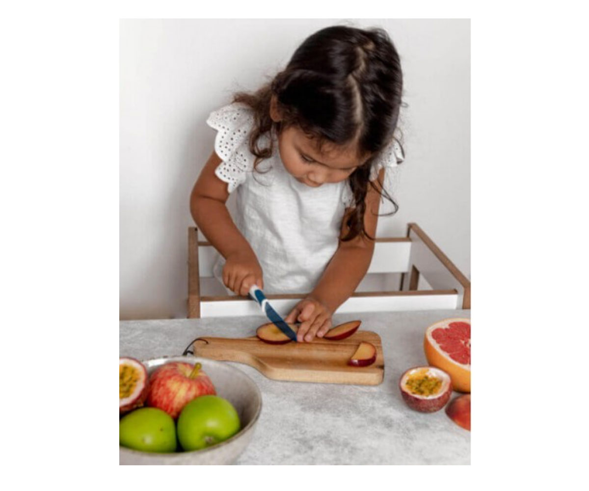 Menina pequena a cortar maçã vermelha num tabuleiro de madeira na cozinha
