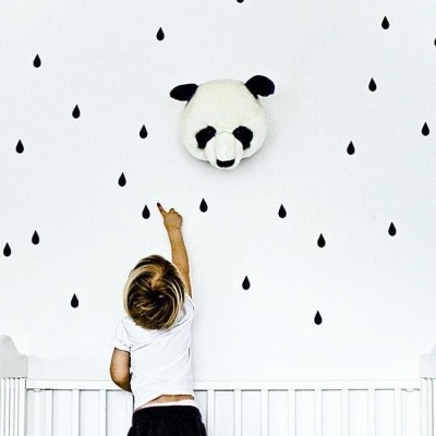 Cabeça de panda em tecido na parede branca com desenhos de gotas pretas e criança a apontar
