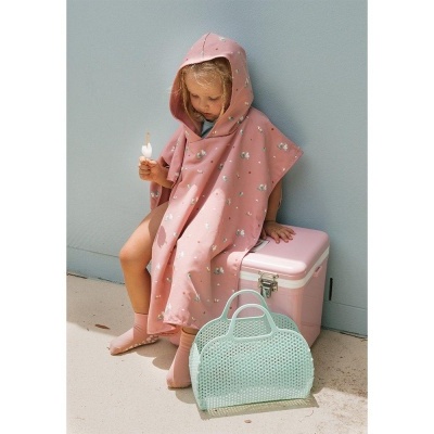 Criança com capa de banho rosa e capuz sentada junto a cooler rosa e bolsa azul clara