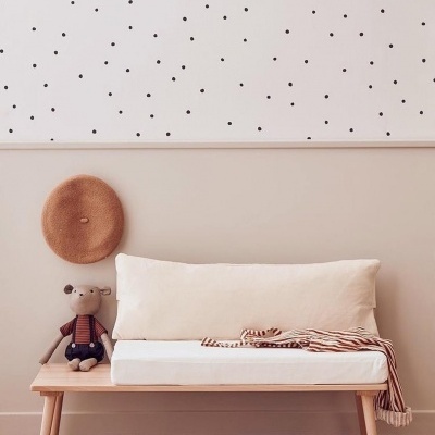 Banco de madeira clara com almofada branca e cobertor listrado, chapéu de palha pendurado na parede com papel de parede de bolinhas