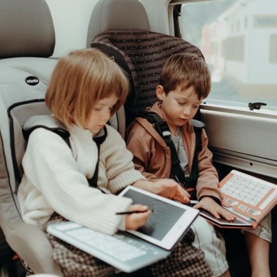 Duas crianças em cadeirinhas de segurança num veículo, ambas com tablets e teclados