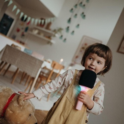 Criança com microfone de brinquedo e urso de peluche numa sala com decoração infantil