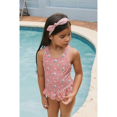 Menina com fato de banho rosa floral e faixa de cabelo rosa junto à piscina
