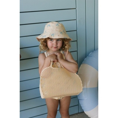 Criança com chapéu e bolsa bege em ambiente azul com boia.