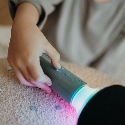 Microfone de brinquedo cinza com luzes coloridas na mão de criança sobre superfície felpuda.