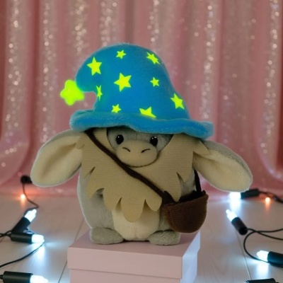 Pelúcia com chapéu azul com estrelas amarelas sobre caixa rosa e luzes brancas