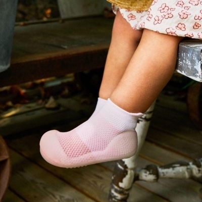 Criança com meias cor-de-rosa com sola antiderrapante sentada num banco de madeira