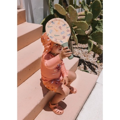 Criança com roupa e chapéu de banho rosa segurando raquete de praia com padrão de animais.