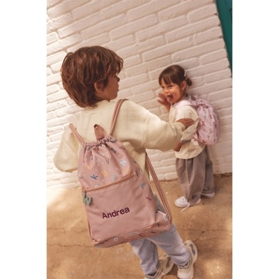 Duas crianças com sacos de cordão cor-de-rosa personalizados contra parede branca